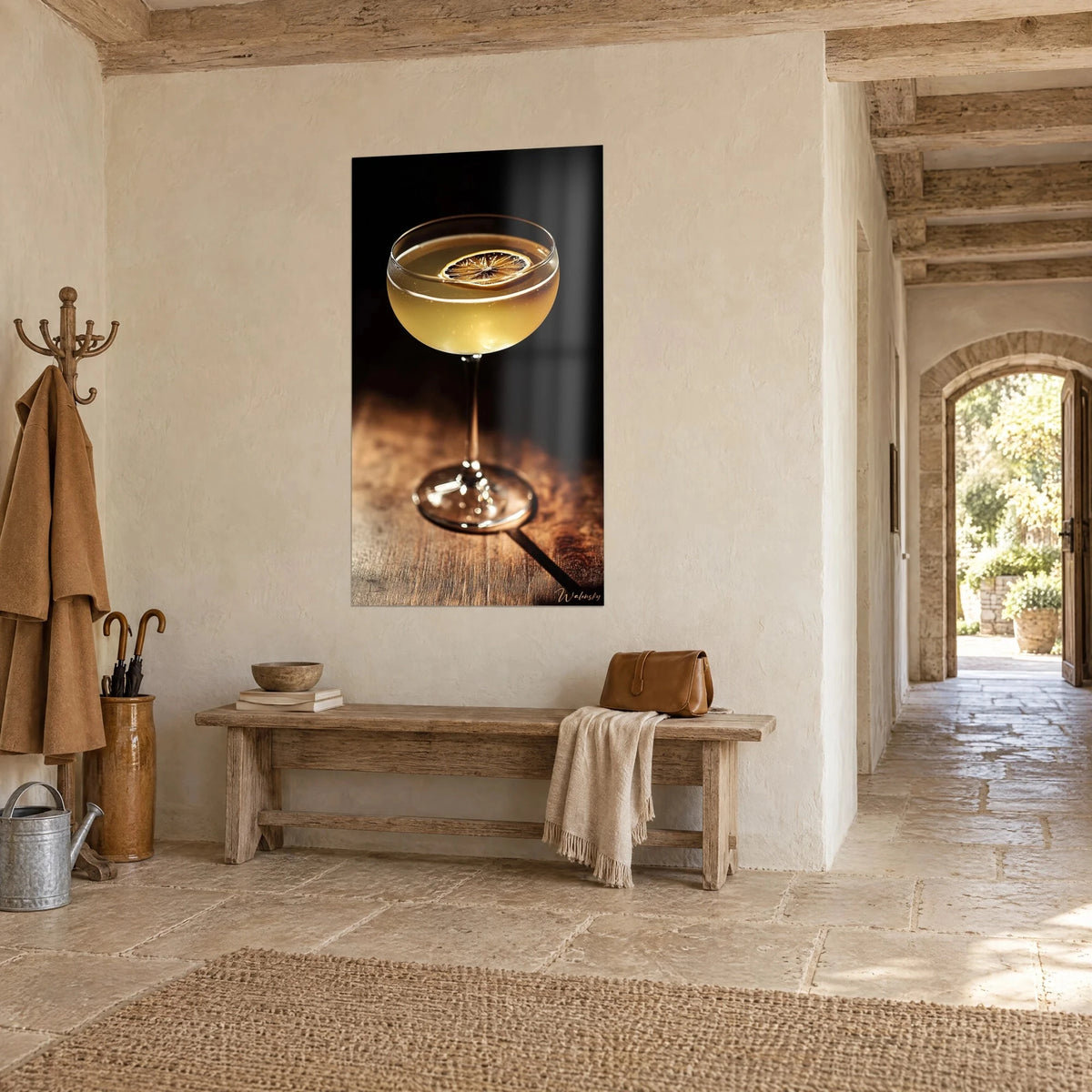 Wall art of a stemmed glass filled with a golden drink, dark background and copper table, hung near a light stone entrance