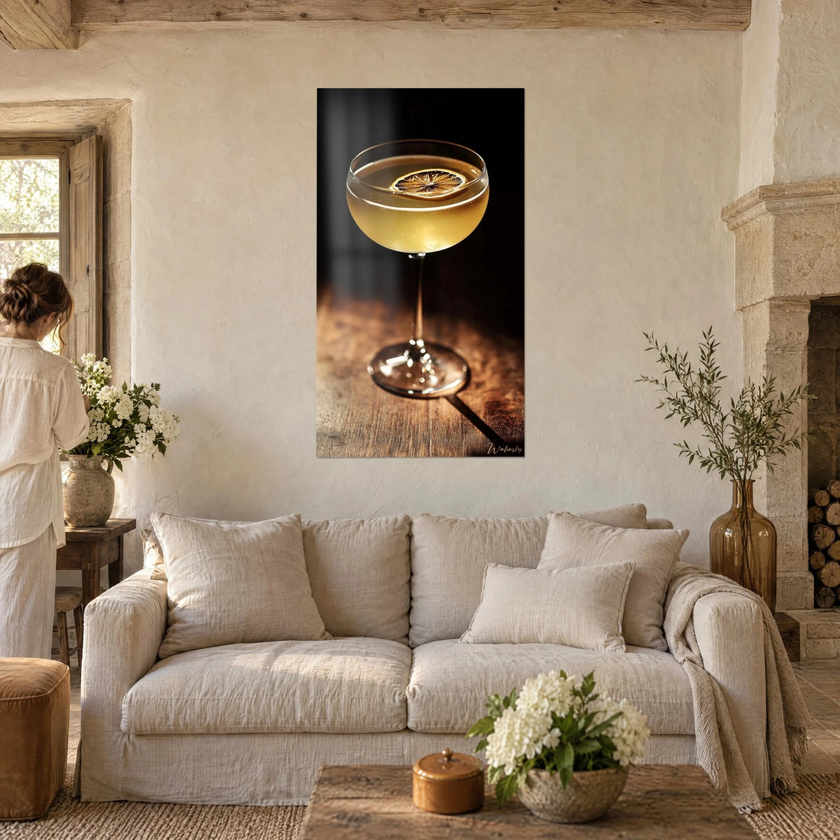 Wall art of an amber cocktail with a dried lemon slice, black background and brown wood, above a sofa in a bright living room