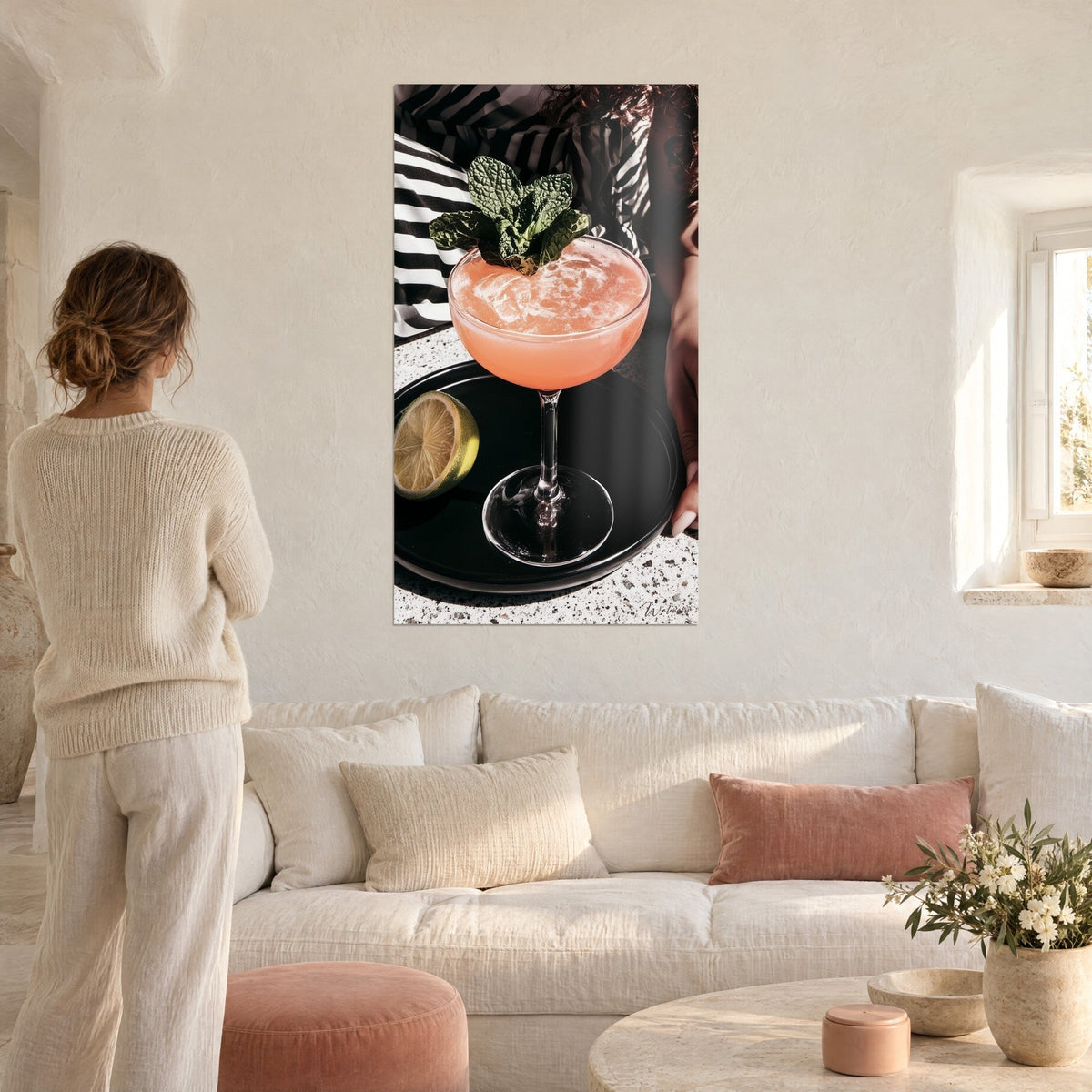 Tableau coupe rose pamplemousse coiffée de menthe géante, plateau noir et citron vert, au-dessus d'un canapé dans un salon lumineux