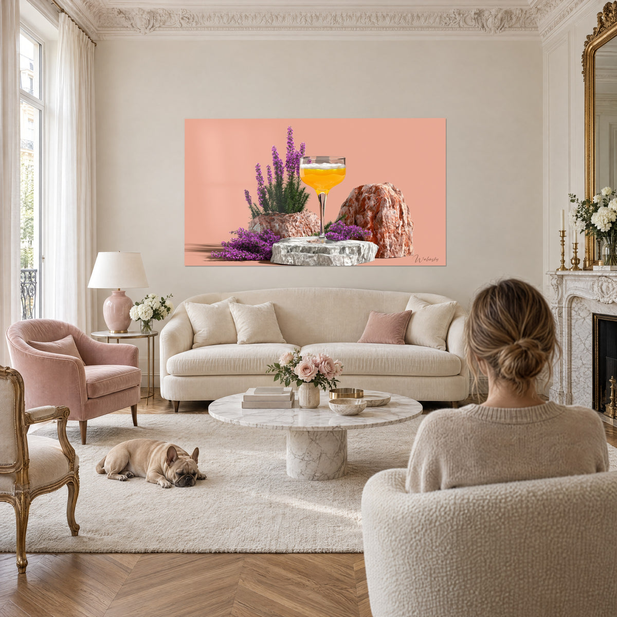 Gemälde Cocktailglas mit bernsteinfarbenem Drink und weißem Schaum, lila Heidekraut auf lachsfarbenem Hintergrund, Bulldogge und Frau von hinten, über einem Sofa in einem hellen Wohnzimmer