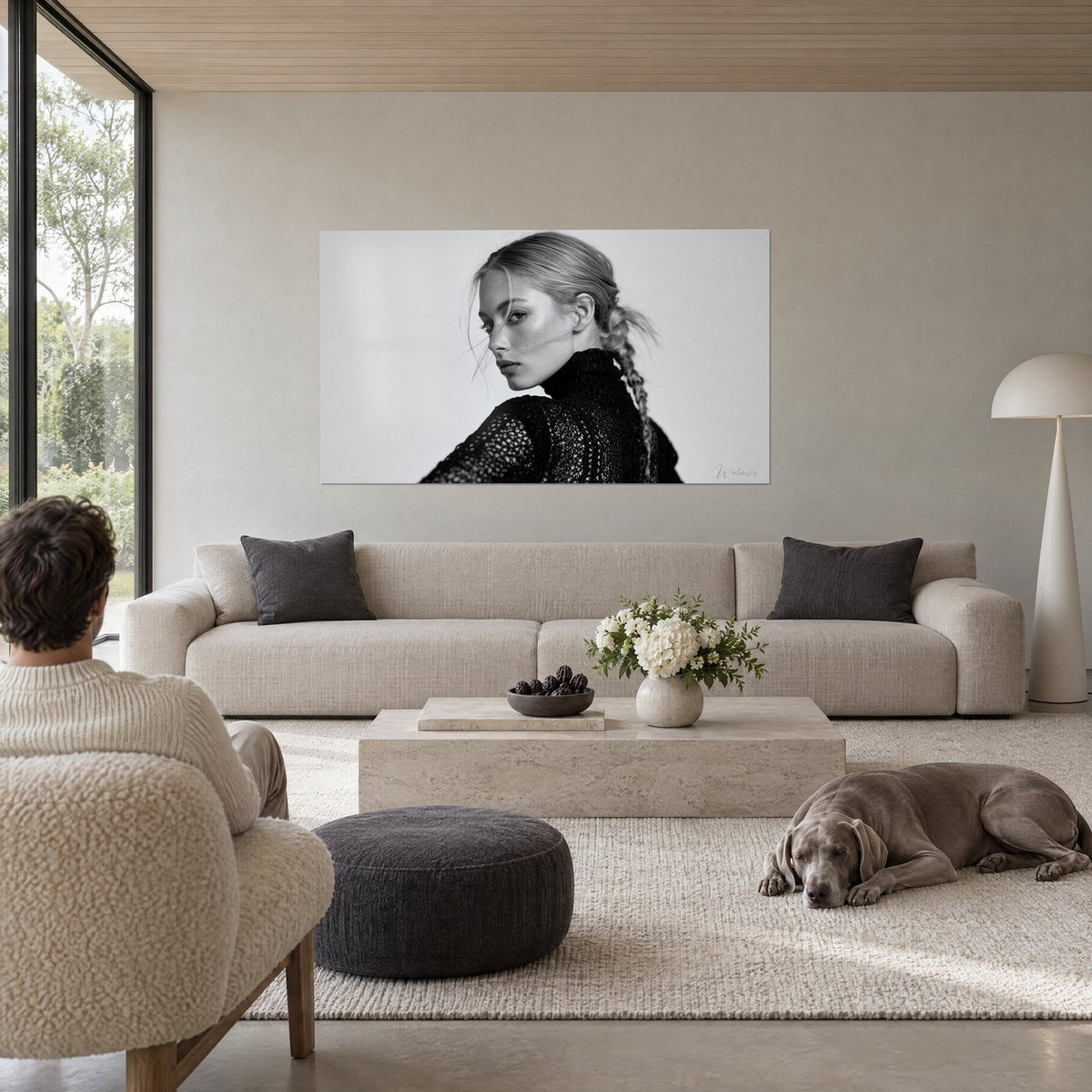 Wall art black and white portrait of a blonde woman with a sideways glance and a braid over her shoulder, above a sofa in a bright living room
