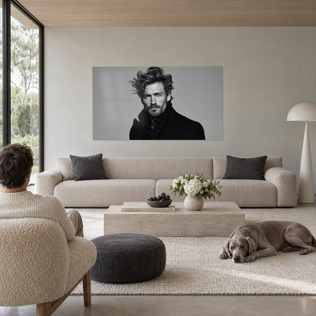 Wall art portrait of a bearded man with tousled locks, black coat against a light grey background, above a sofa in a bright living room