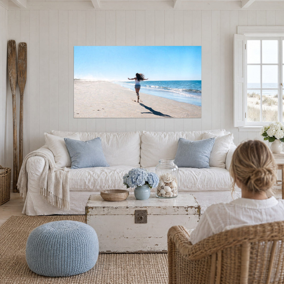Tableau femme courant pieds nus, bras ouverts, cheveux au vent sur sable clair et mer bleue, au-dessus d'un canapé dans un salon lumineux