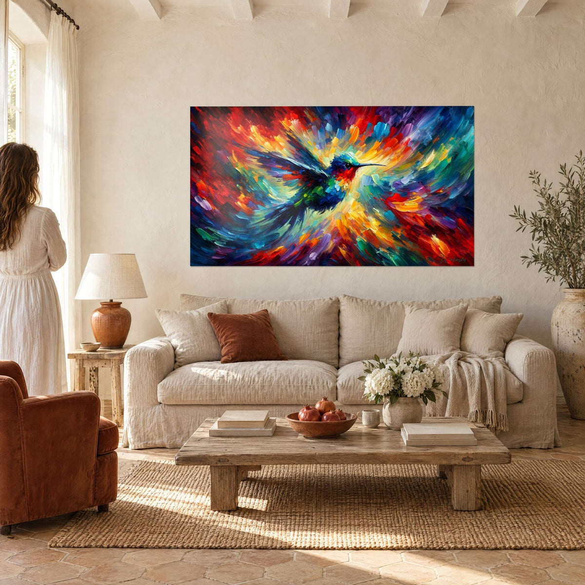 Tableau colibri en vol, plumage bleu nuit et gorge rouge, fond orange vif, femme de dos, au-dessus d'un canapé dans un salon lumineux