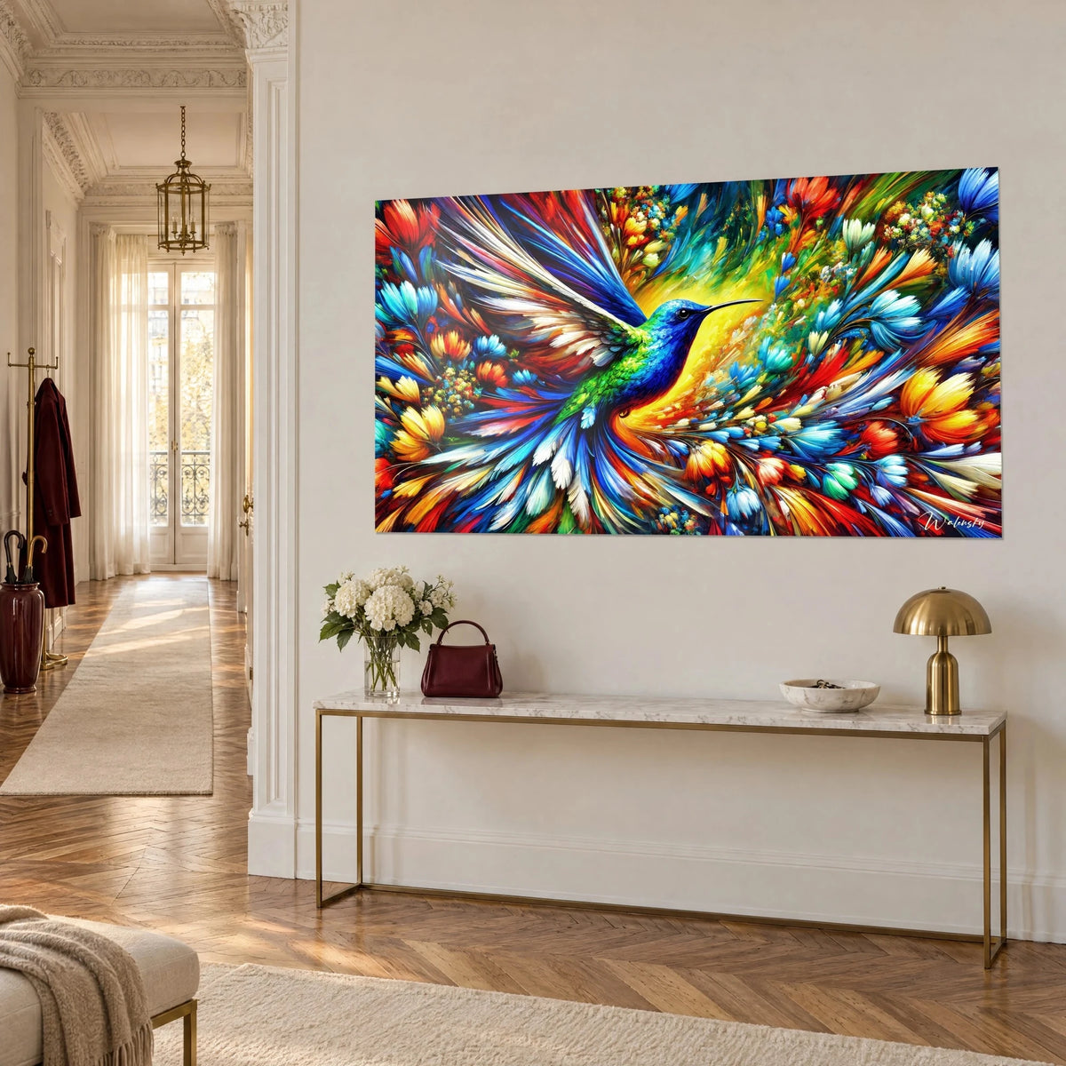 Tableau oiseau-mouche au bec noir fin, gorge émeraude et corolles rouges et orangées éclatantes, vue de trois-quarts sur un mur crème