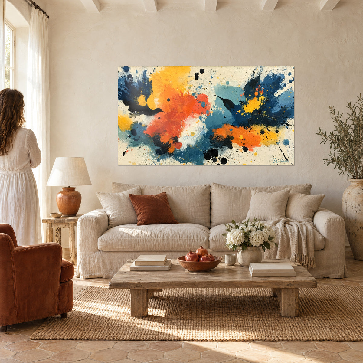 Tableau colibris silhouettés en plein vol, éclaboussures orange et jaune sur fond bleu marine, au-dessus d'un canapé dans un salon lumineux