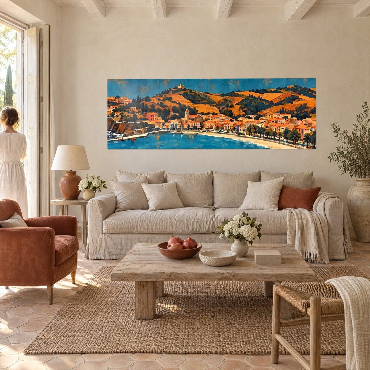 Tableau village côtier panoramique aux toits orange et mer bleue, collines ocre, une femme de dos, au-dessus d'un canapé dans un salon lumineux