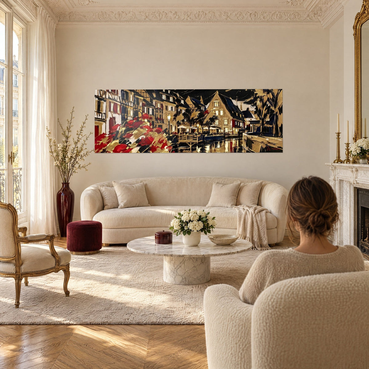 Schilderij nachtelijke gracht met gouden en karmijnrode gevels, dikke penseelstreken, vrouw van achteren boven een bank in een lichte woonkamer