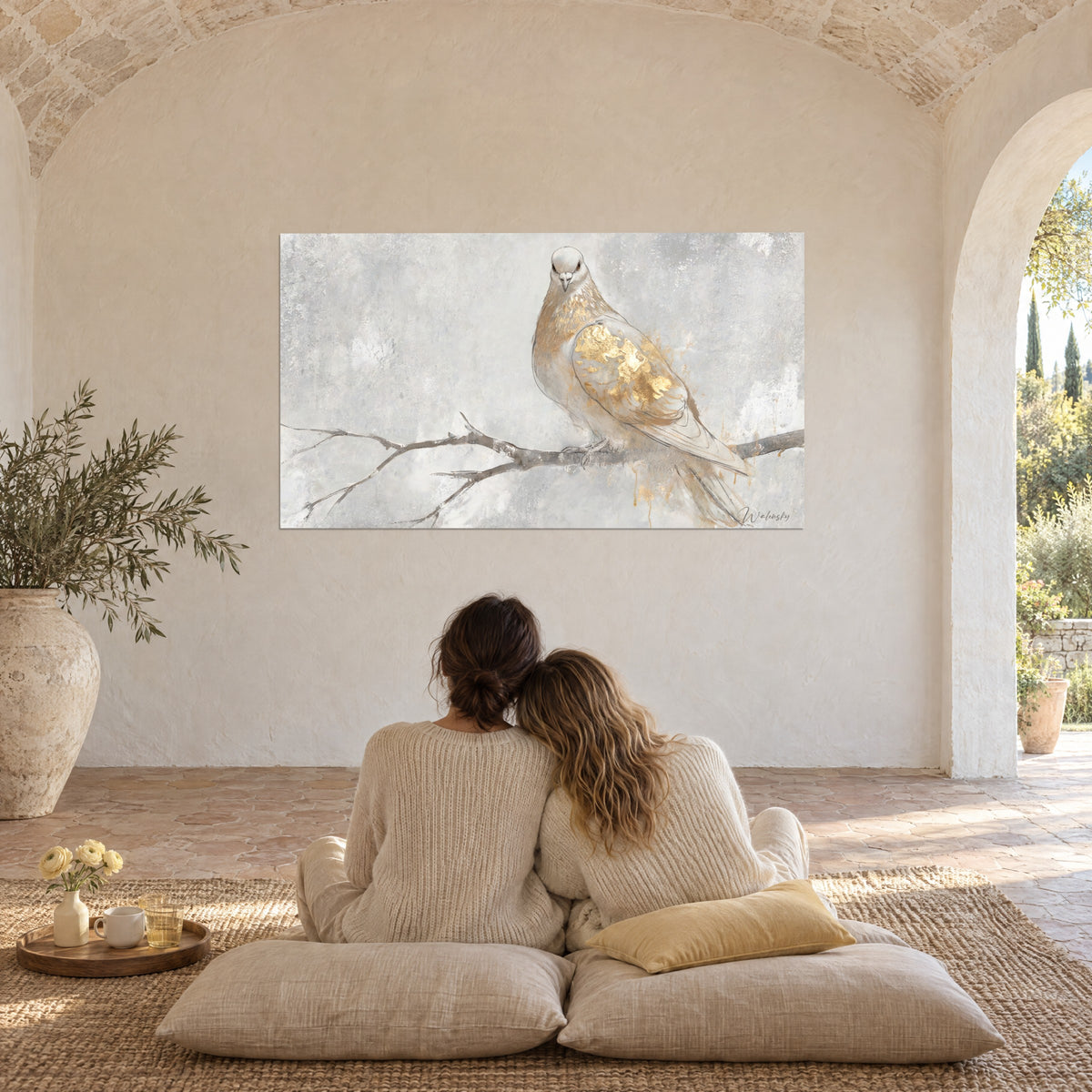 Tableau colombe perchée, plumes blanches et or, fond gris nuancé, devant un couple de dos sur des coussins dans un mas provençal