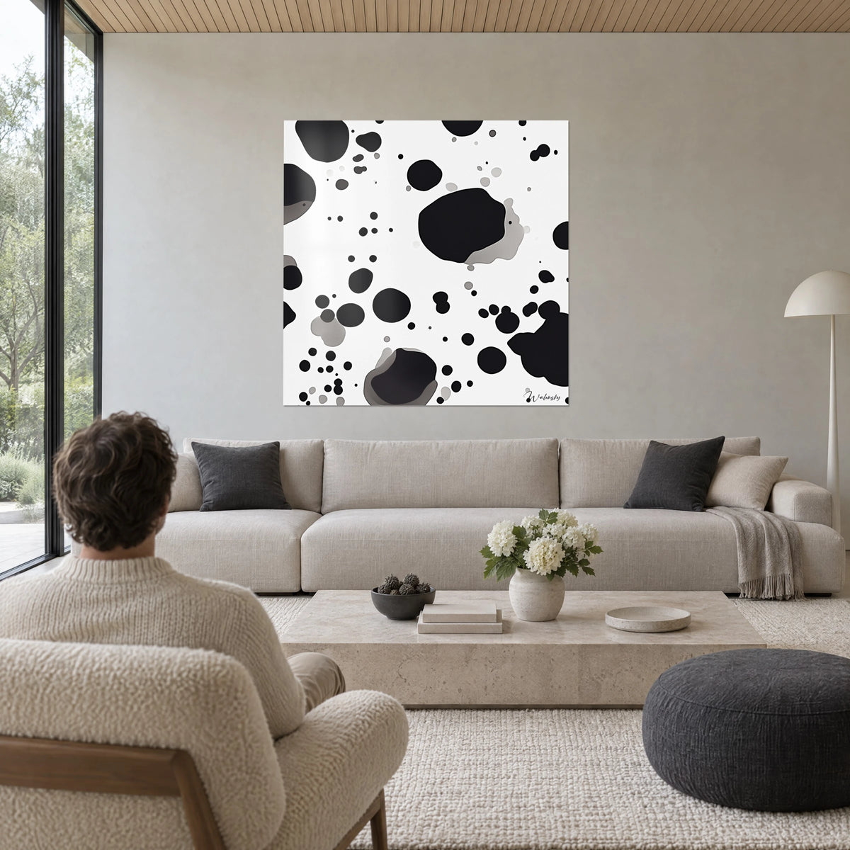 Tableau taches d'encre noires sur fond blanc, grosse tache centrale et petits points, au-dessus d'un canapé dans un salon lumineux