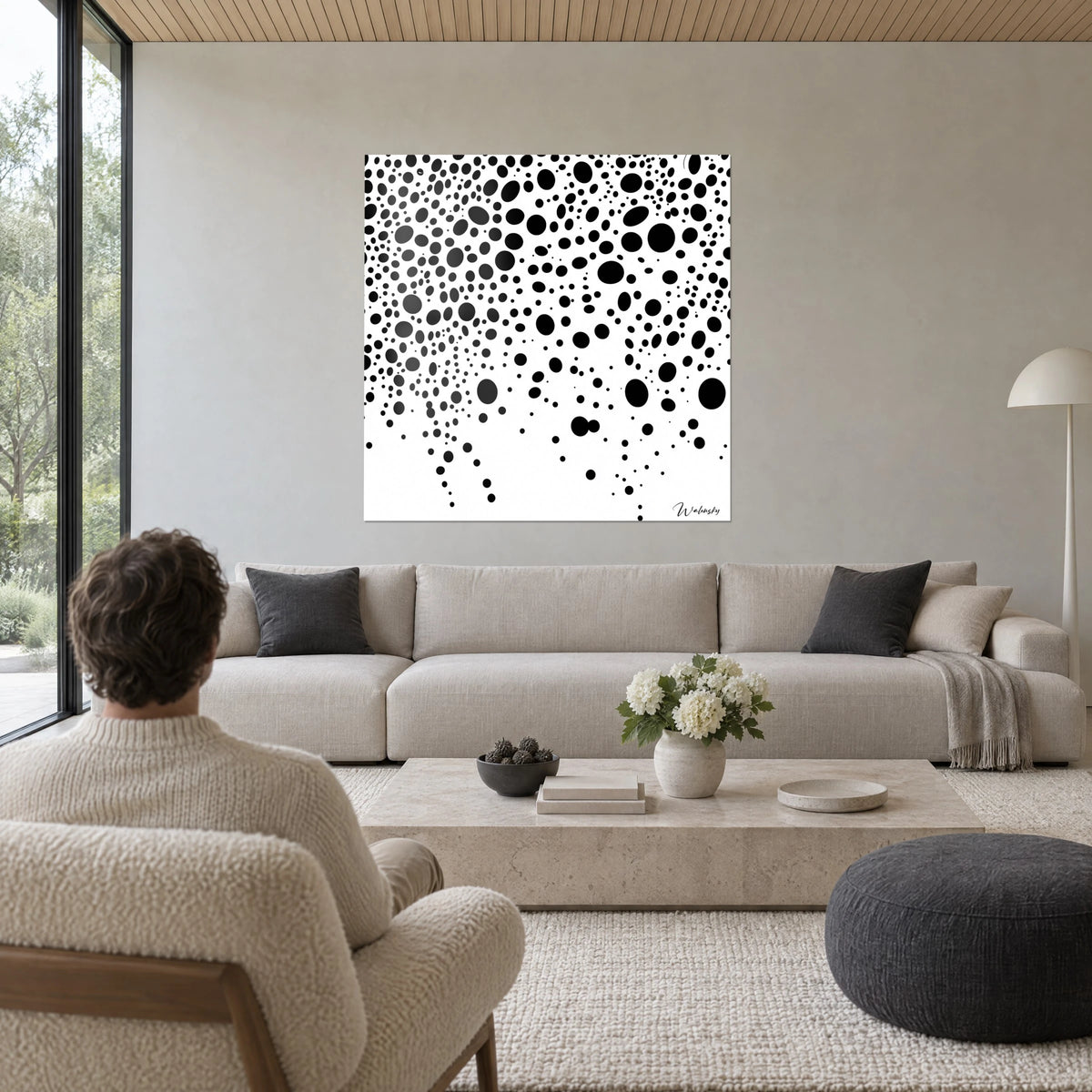 Tableau pois noirs en pluie sur fond blanc, grosses taches ovales en bas à droite, homme de dos, au-dessus d'un canapé dans un salon lumineux