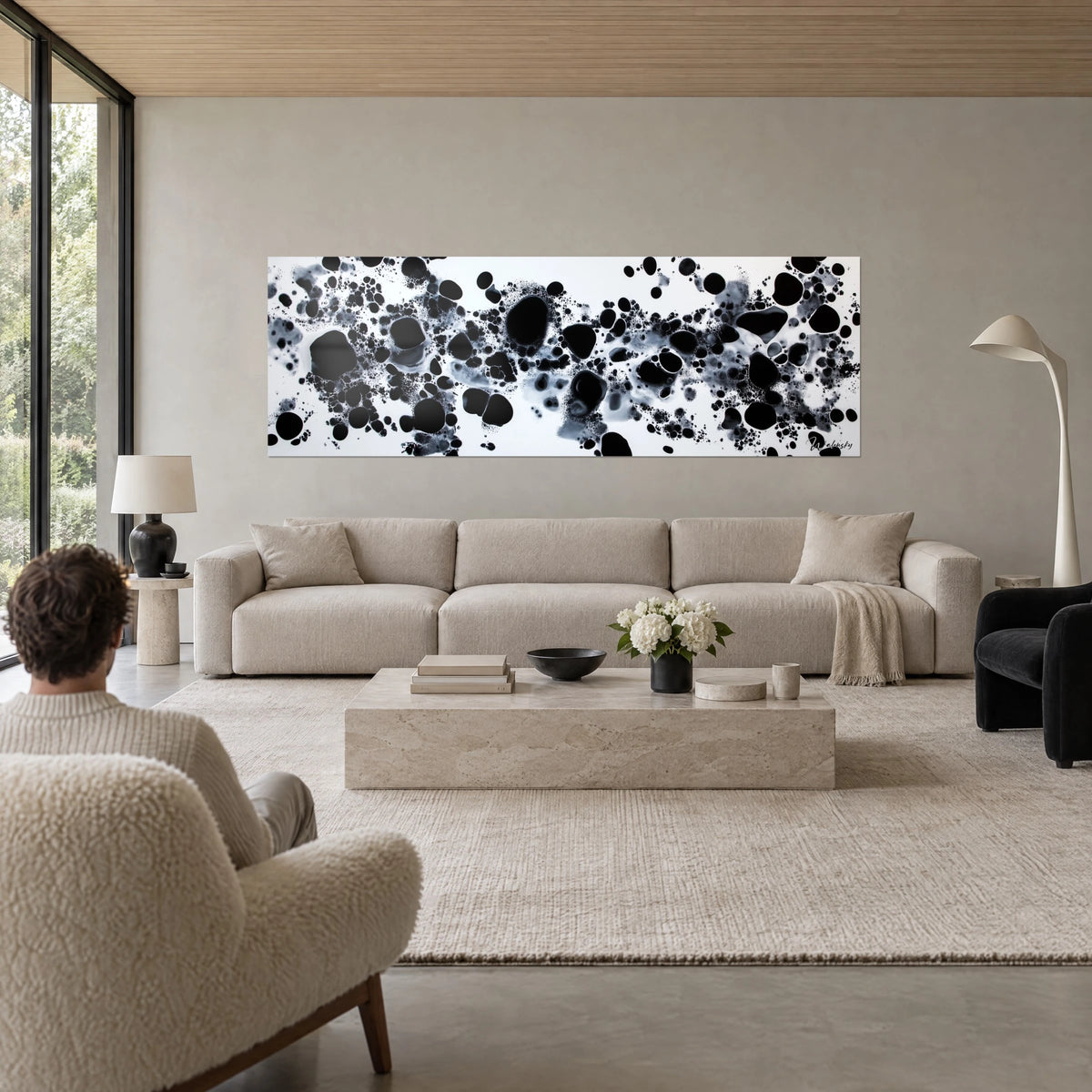 Wall art nebula of black ink splashed into droplets on a white background, shades of grey, above a sofa in a bright living room