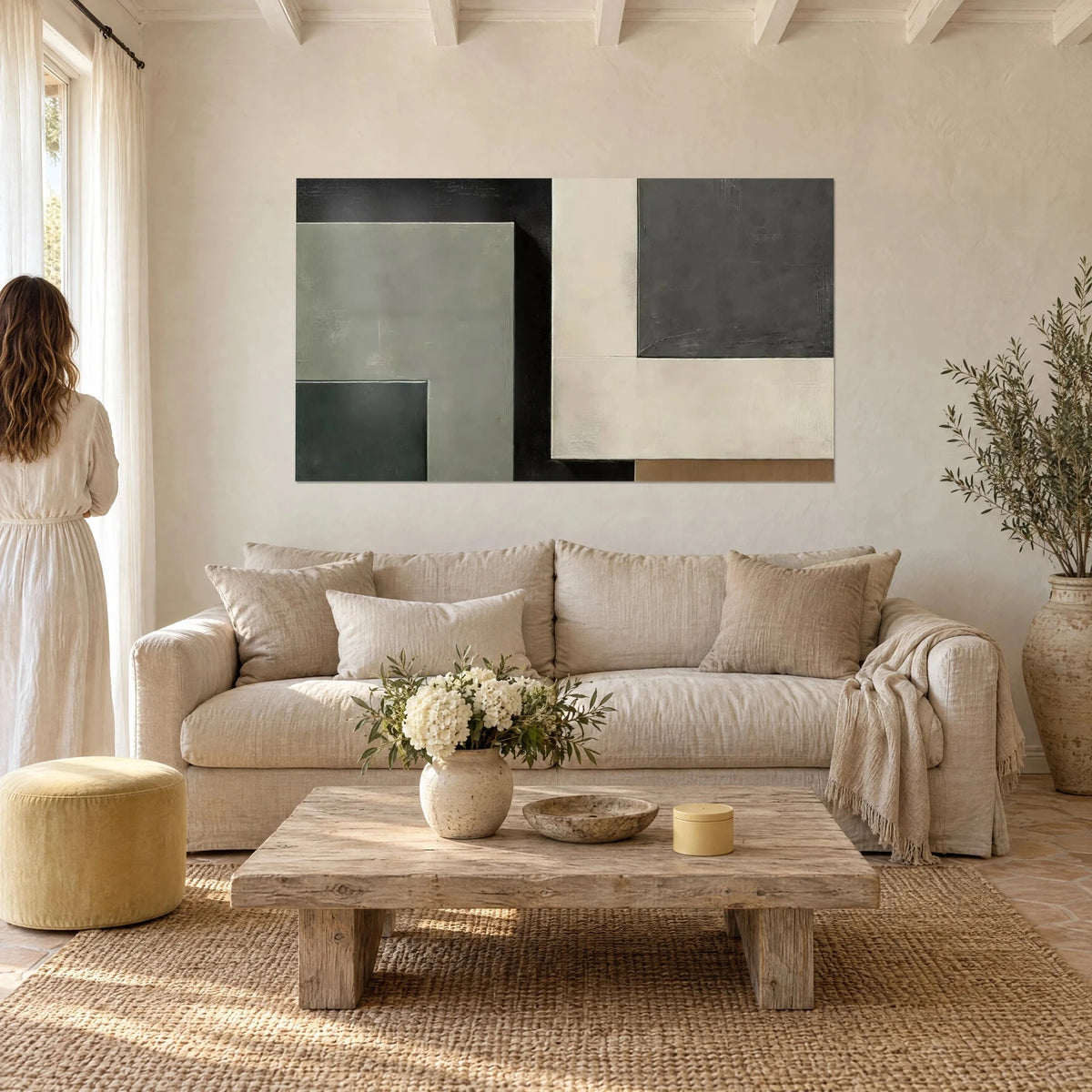 Schilderij composities van saliegroene, zwarte en crèmekleurige vierkanten, twee personen met de rug naar de kijker, boven een bank in een lichte woonkamer