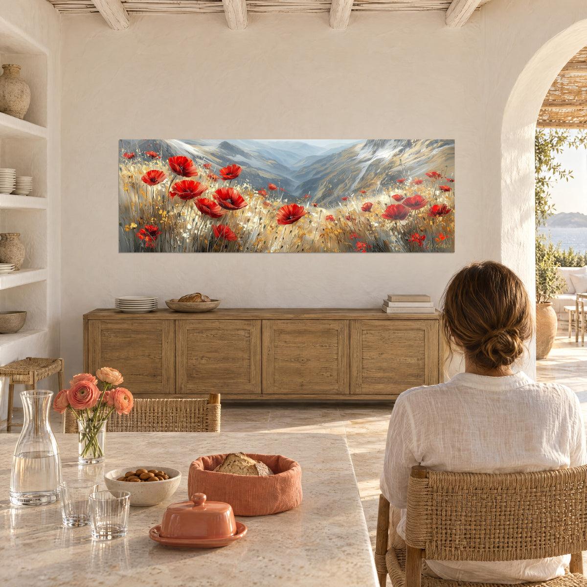 Wall art of an alpine meadow dotted with red blossoms, honey-yellow grasses and an azure valley, woman seen from behind seated at a table in a vaulted kitchen