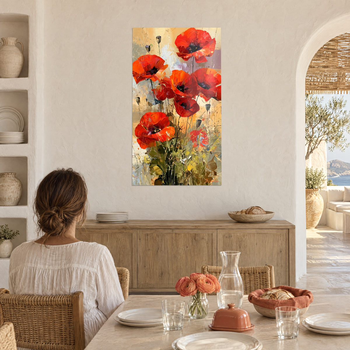 Quadro campo di papaveri arancioni punteggiati di giallo, donna di spalle seduta a un tavolo in una cucina bianca con cestini intrecciati