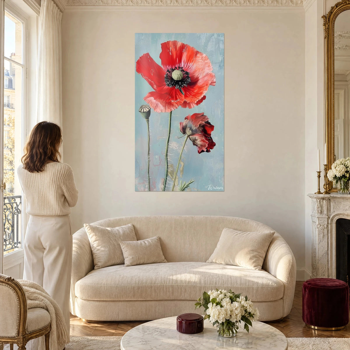 Schilderij grote klaproos in vermiljoenrood en grijsgroene knop op lichtblauwe achtergrond, vrouw van achteren, boven een bank in een lichte woonkamer