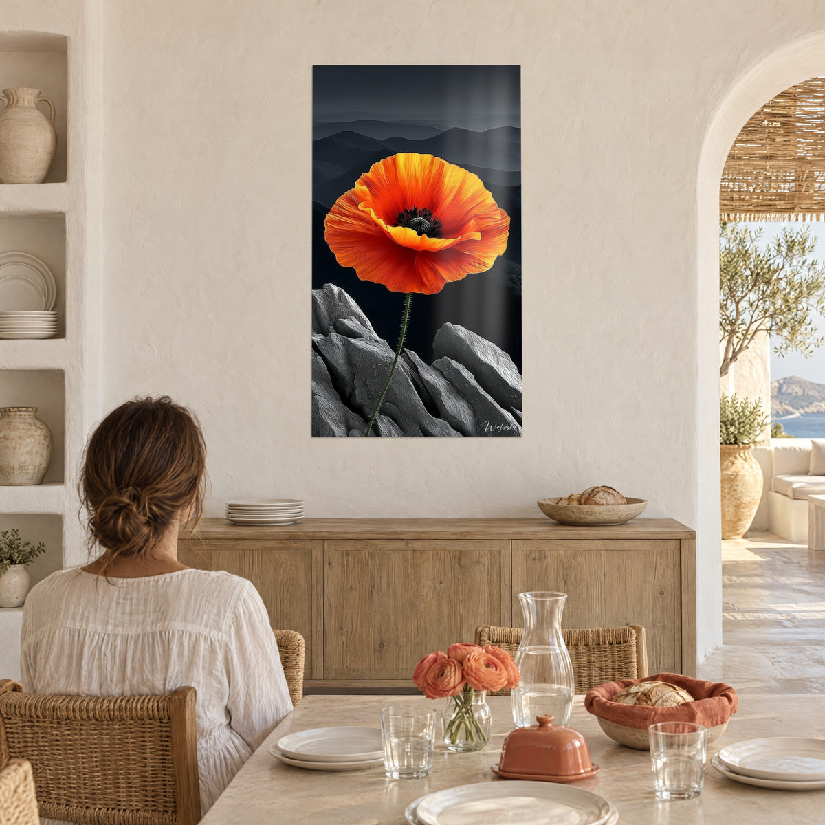 Schilderij grote oranjegele bloem op zilvergrijze rotsblokken, vrouw van achteren aan tafel in een witte gewelfde keuken