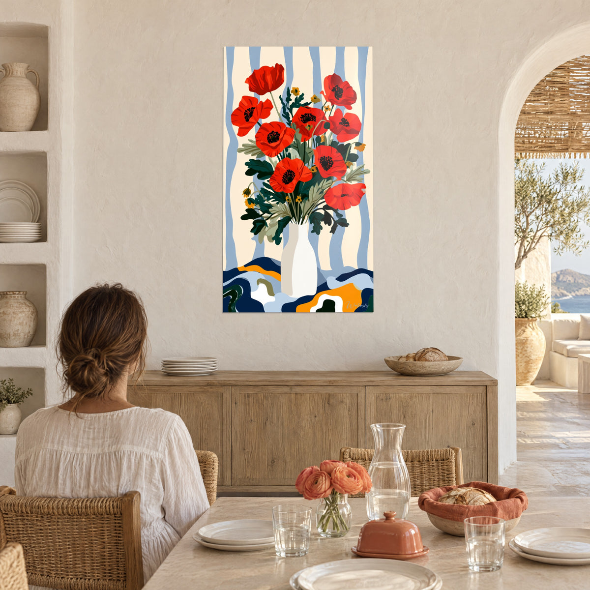 Wall art orange poppies with black centres on pale blue striped background, woman seen from behind seated at a table near a light wood sideboard