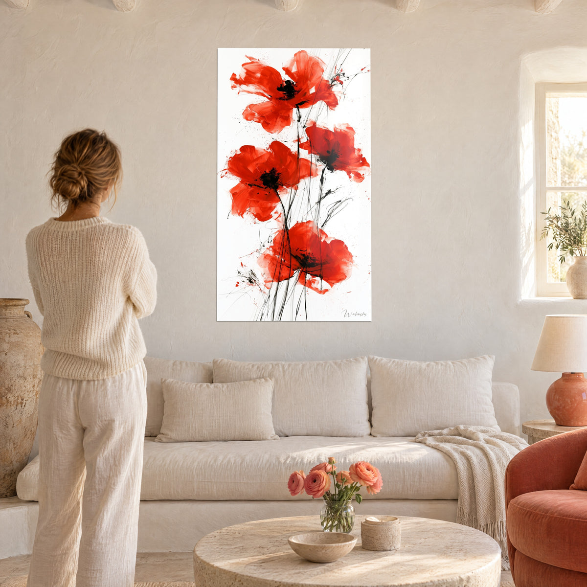 Quadro con quattro papaveri scarlatti dal cuore nero, steli sottili e fondo bianco, donna di spalle sopra un divano in un soggiorno luminoso