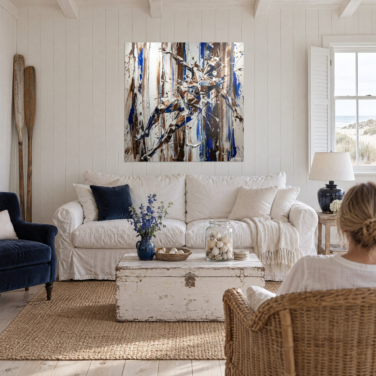 Wall art silhouette in shattered cobalt blue and brown shards, white drips, hanging above a sofa in a bright living room