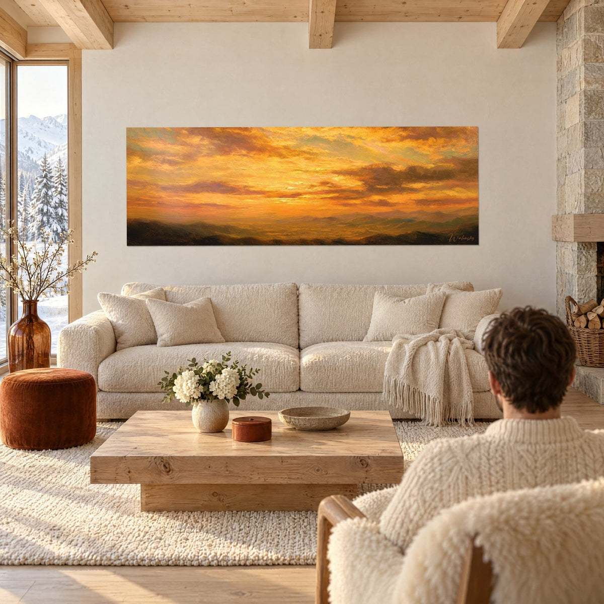 Wall art blazing sky in orange and amber over dark ridges, a person seen from behind, above a sofa in a bright living room
