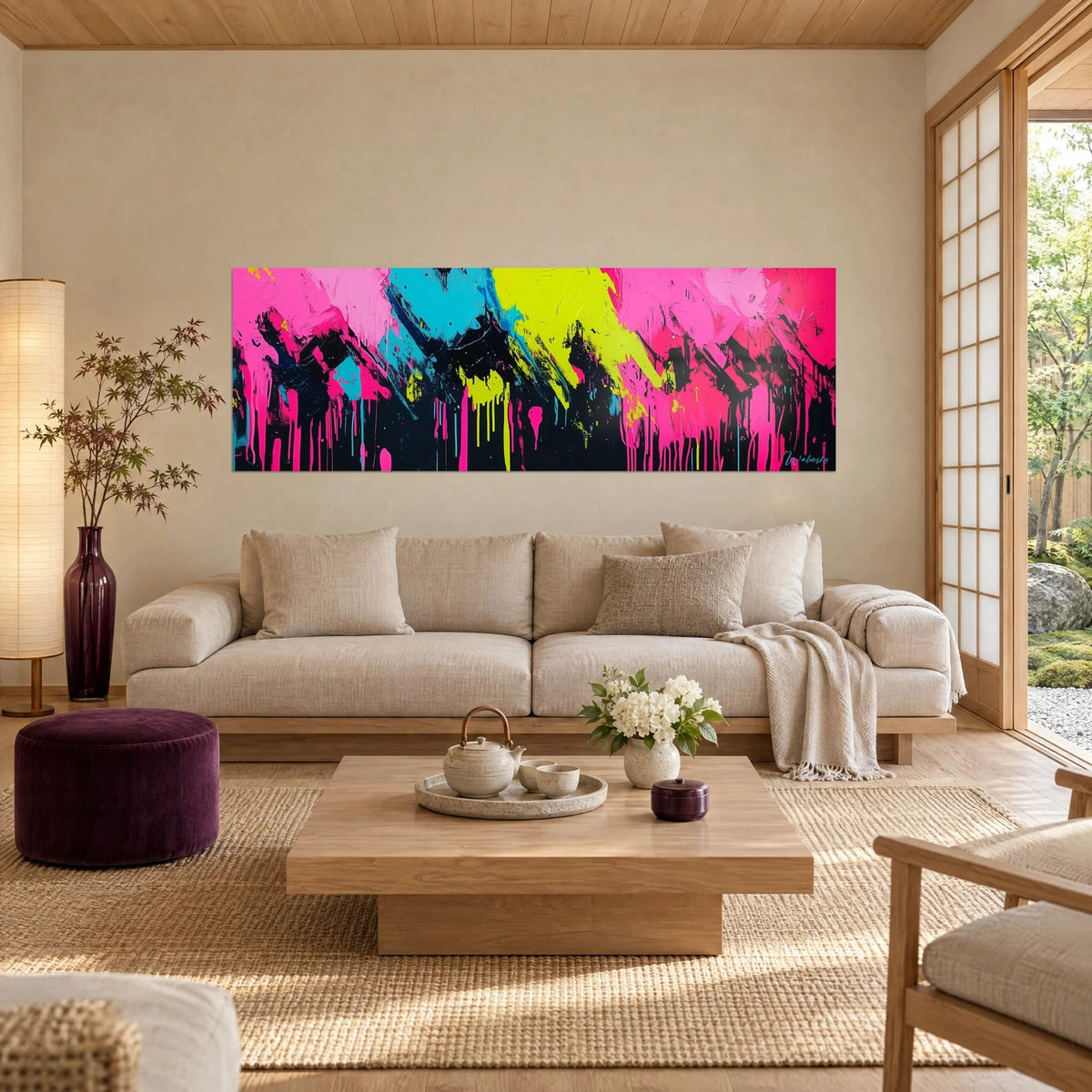 Tableau éclaboussures de peinture rose fluo, turquoise et jaune acide sur fond noir, au-dessus d'un canapé dans un salon lumineux