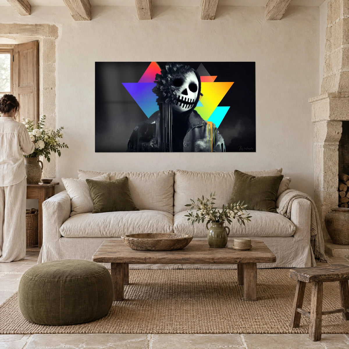 Gemälde Totenkopf in Weiß mit schwarzer Blumenmaske, Dreiecke in Regenbogenfarben Violett und Gelb, über einem Sofa in einem hellen Wohnzimmer