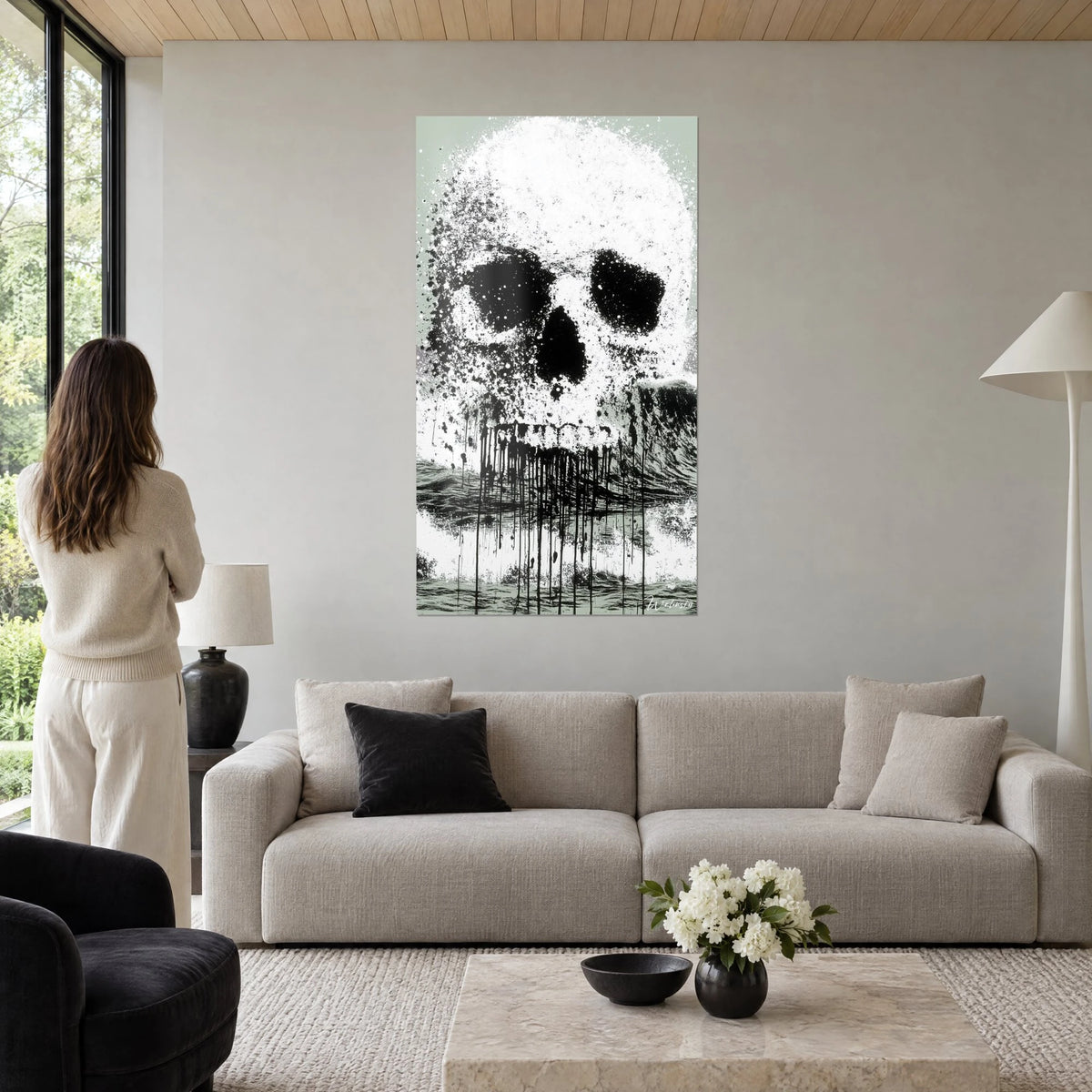 Gemälde Schädel weiß gespritzt, schwarze Augenhöhlen und Tintenläufe auf hellgrünem Grund, über einem Sofa in einem lichtdurchfluteten Wohnzimmer