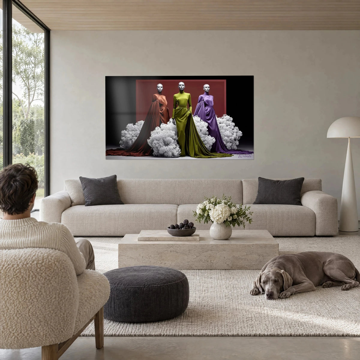 Schilderij drie mannequins met verchroomde schedels in roestkleurige, olijfgroene en paarse satijnen jurken, boven een bank in een lichte woonkamer