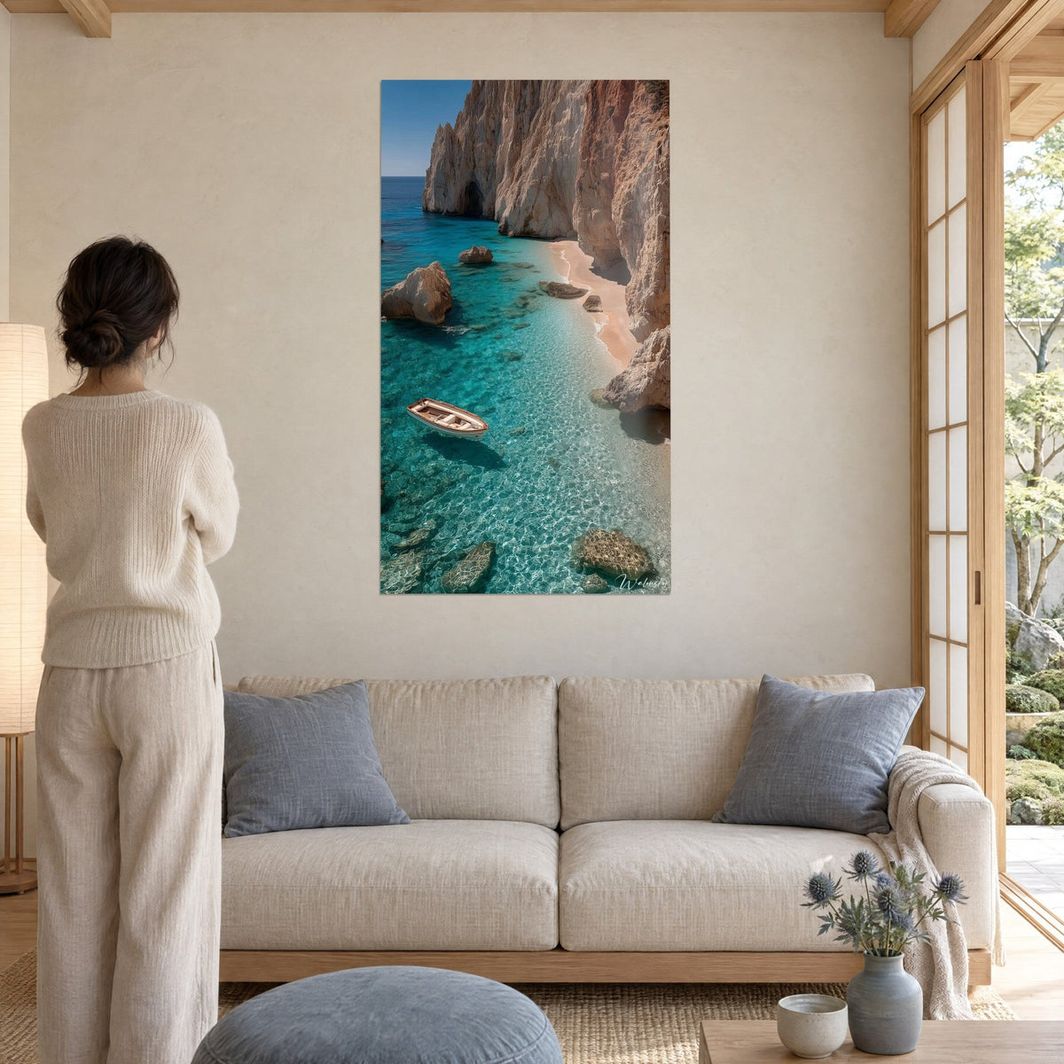 Wall art of a Mediterranean cove with turquoise waters, ochre cliffs and a white boat, woman seen from behind, above a sofa in a bright living room