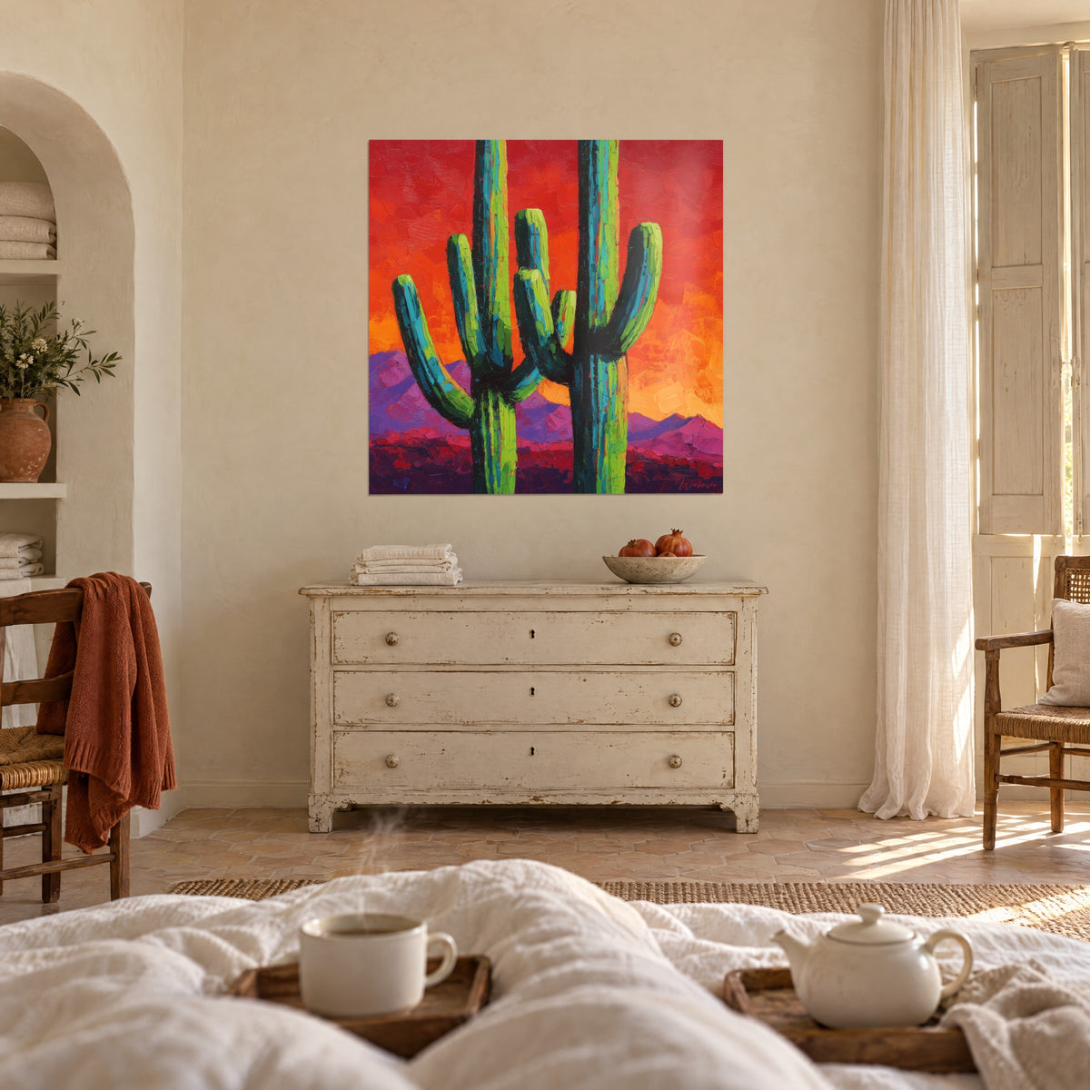 Tableau deux saguaros élancés, verts et bleu canard, sur un coucher de soleil rouge orangé, au-dessus d'un lit dans une chambre claire