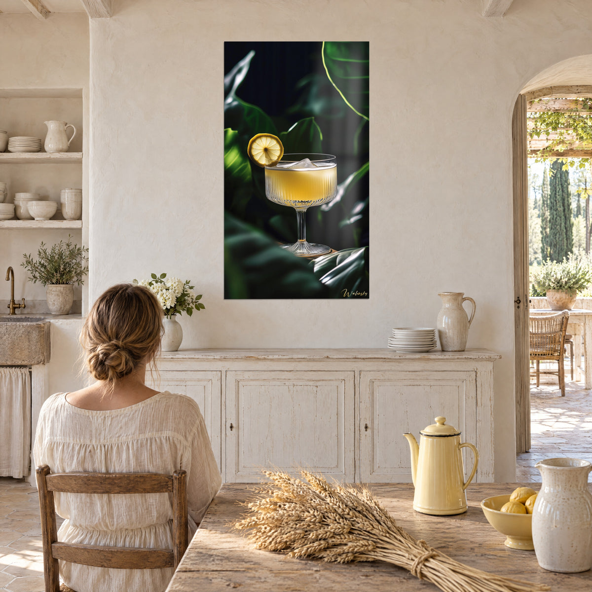Tableau cocktail au citron sur fond de feuilles vert foncé, coupe à pied fin et glaçon, mur beige, jeune femme de dos à table
