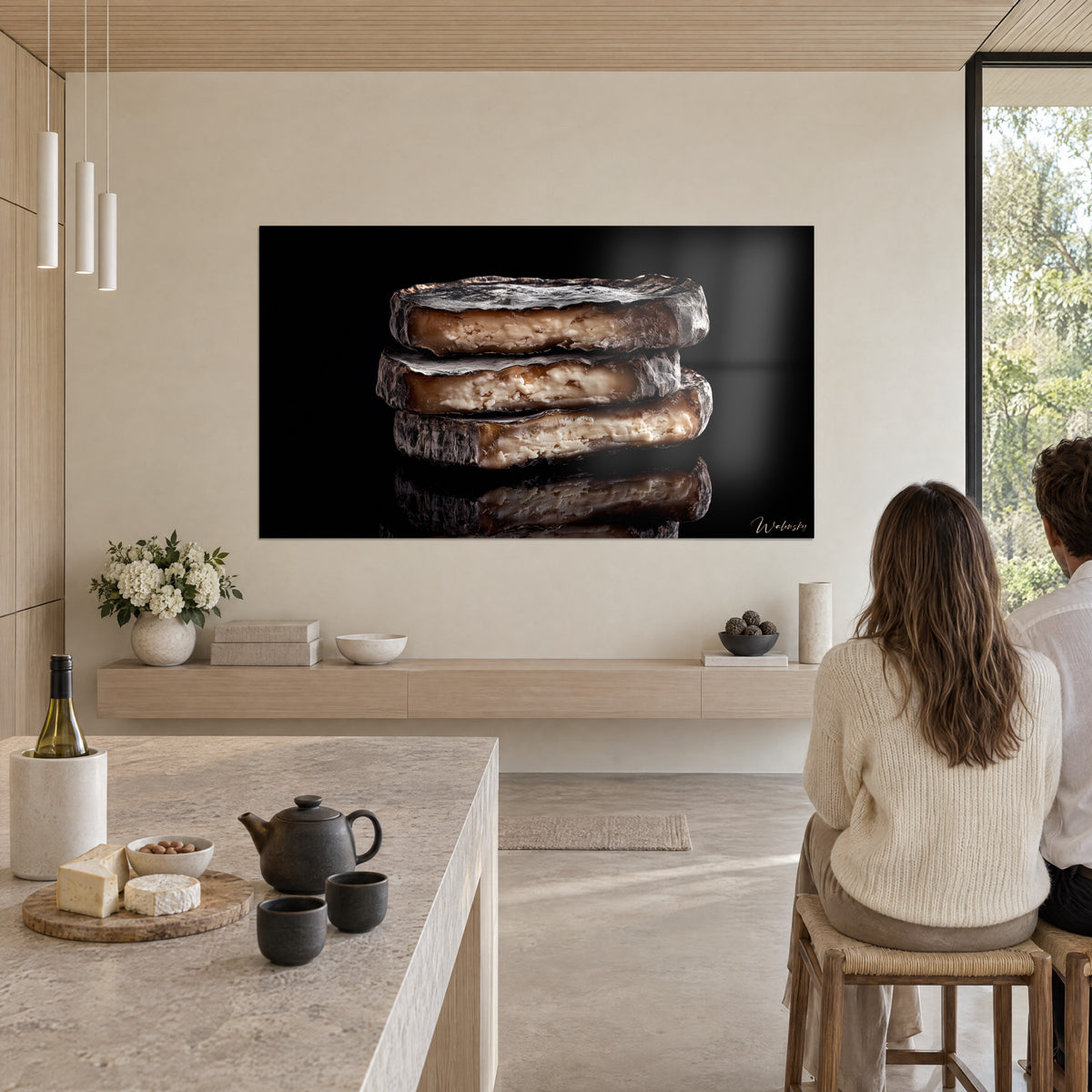 Wall art stack of three cheeses with ash-grey rind and browned ivory paste, glossy black reflection, facing a light stone kitchen island, Walensky