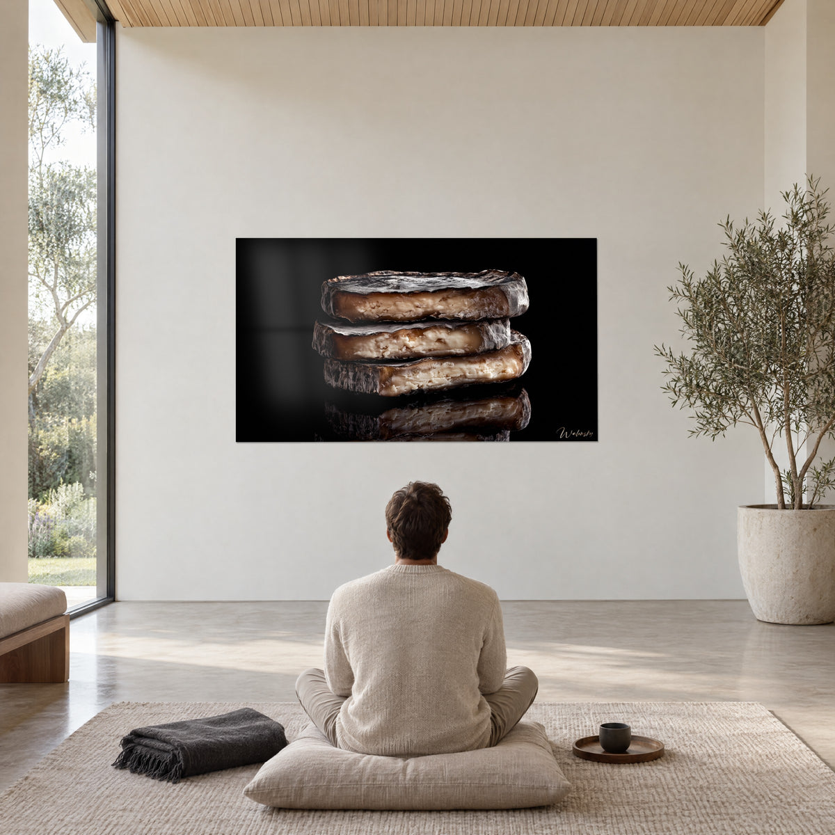 Wall art three cheese cakes with charcoal rind and grainy ivory crumb, black background, watched by a man seated on a cushion, Walensky