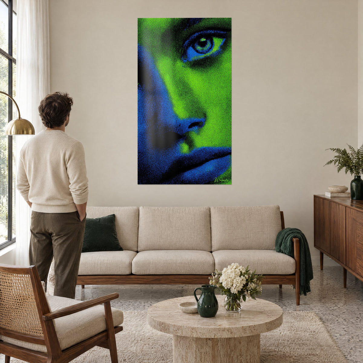 Tableau visage mi-vert mi-bleu au regard perçant, trame pointillée, un homme de dos, au-dessus d'un canapé dans un salon lumineux