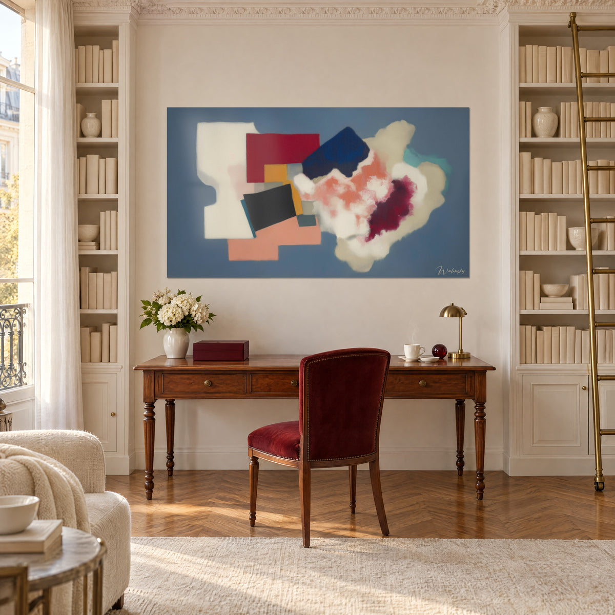 Quadro arte astratta in carte ritagliate rosse, blu navy e corallo su grigio azzurro, sopra una scrivania in legno tra due librerie