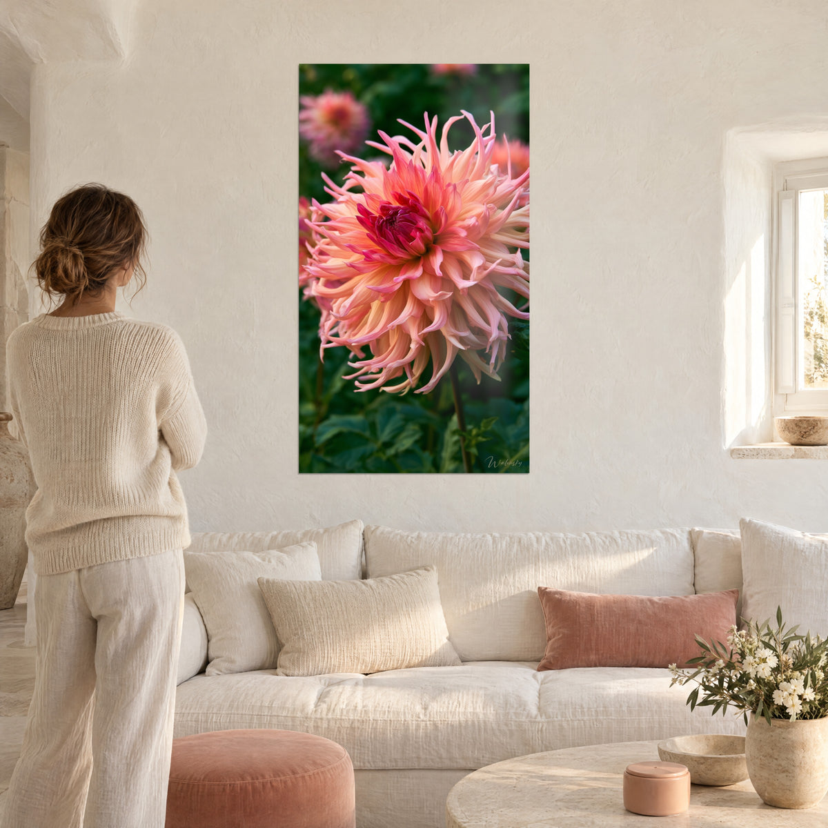 Schilderij cactusdahlia in perzik en magenta met slanke bloemblaadjes, karmijnrood hart, vrouw van achteren, boven een bank in een lichte woonkamer