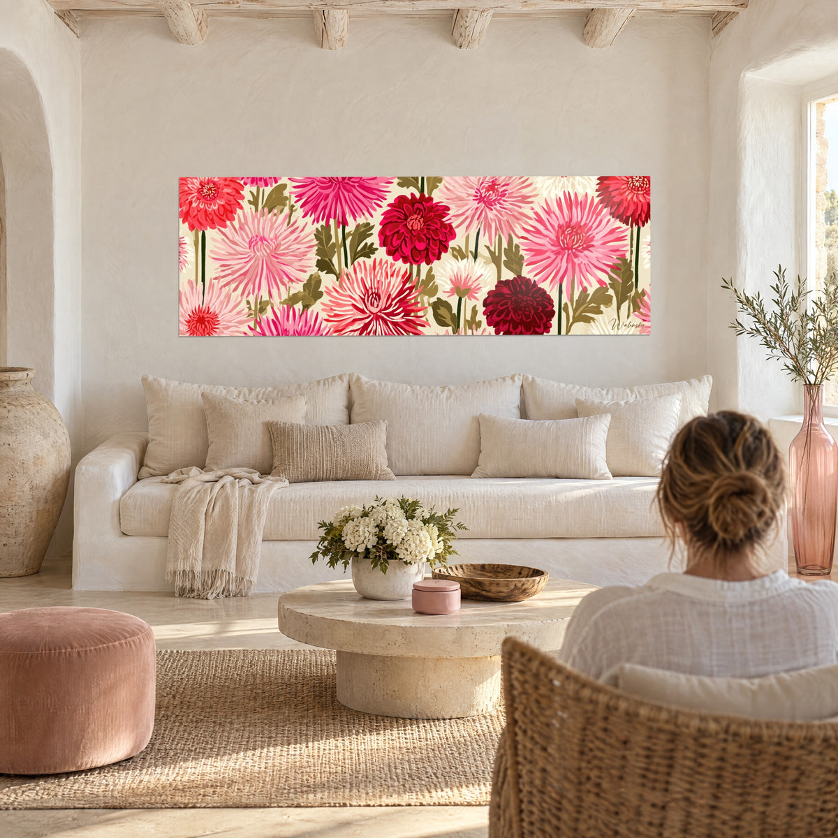 Wall art pink and garnet dahlias with pointed petals on a cream background, a woman seen from behind above a sofa in a bright living room