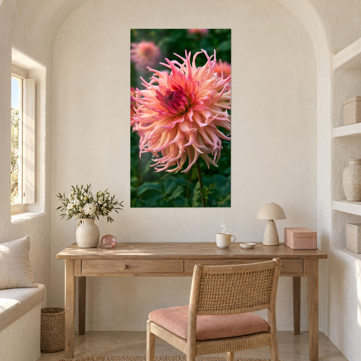 Schilderij bloempompon in zalm en magenta, fijne spiraalvormige bloemblaadjes boven wazig groen, opgehangen boven een bureau van licht hout