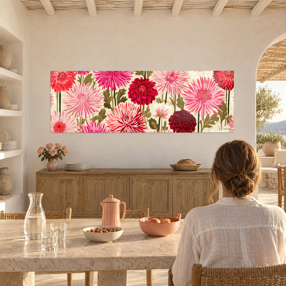 Wall art field of bubblegum pink, cherry red and garnet dahlias, a woman seen from behind seated at a table in front of a light wood sideboard