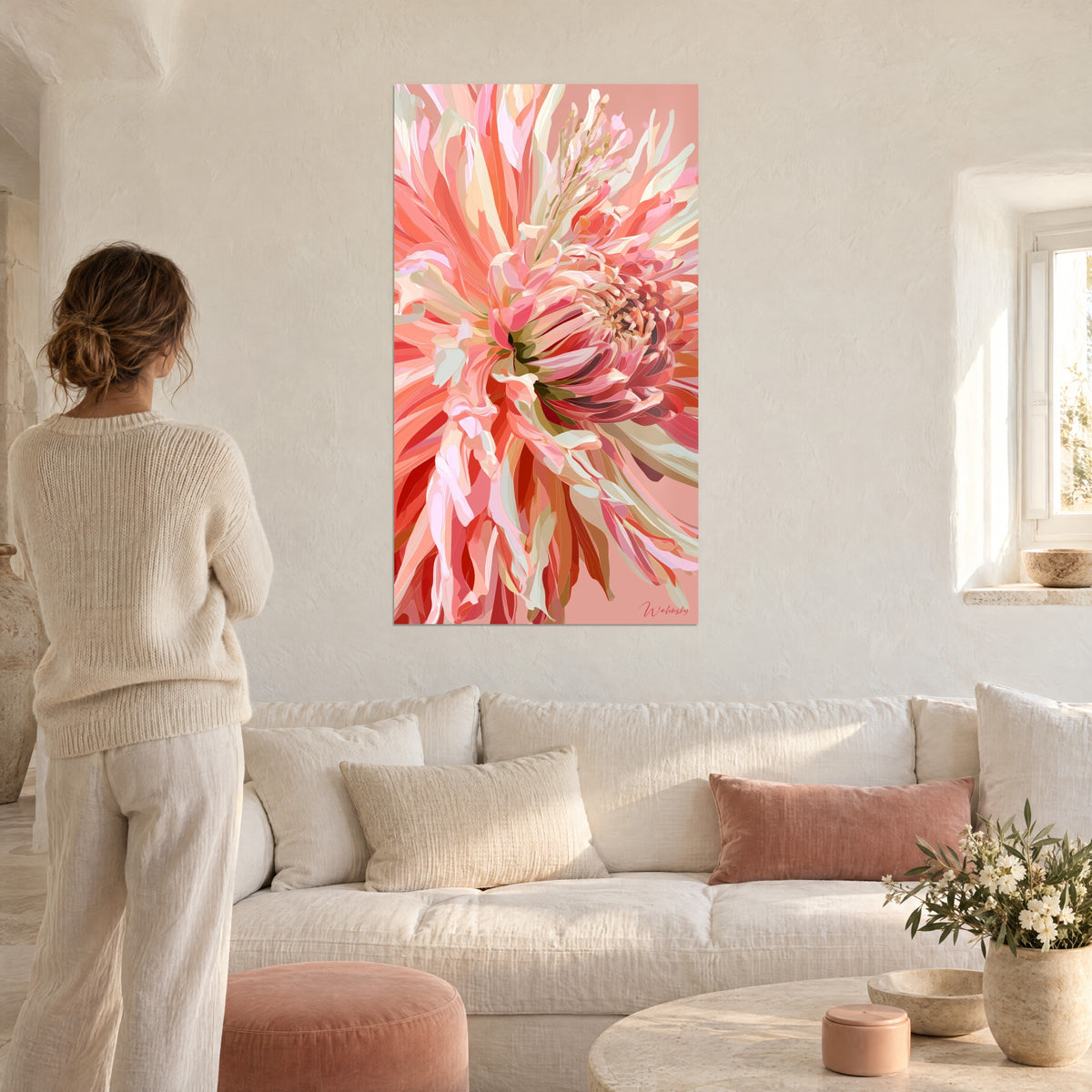 Quadro dalia corallo dai petali arricciati, cuore rosso vivo su fondo rosa cipria, persona di spalle sopra un divano in un soggiorno luminoso
