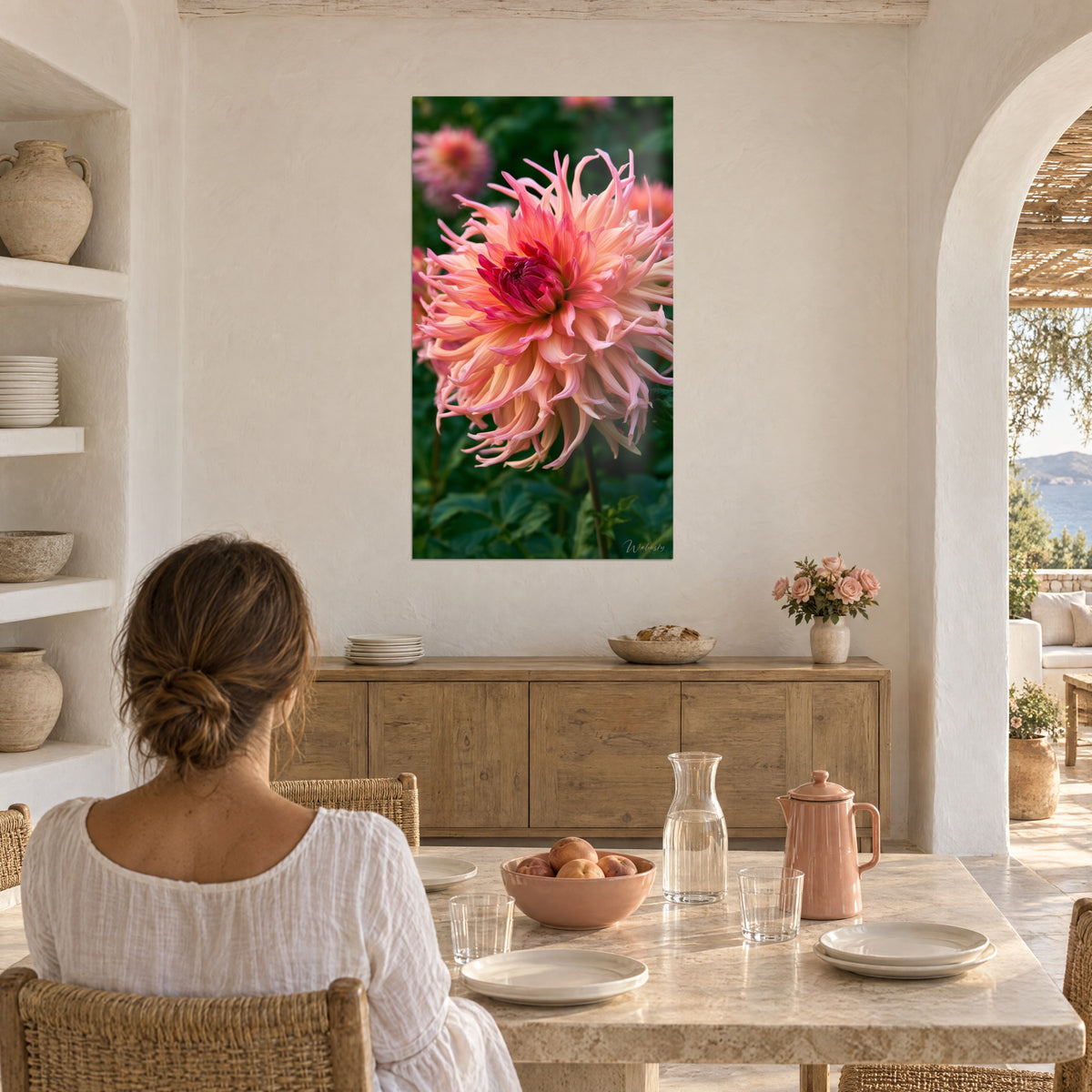 Schilderij bloemkroon in abrikoos en fuchsia met opgerolde punten, gezien door een vrouw van achteren aan tafel, in een Mediterrane keuken