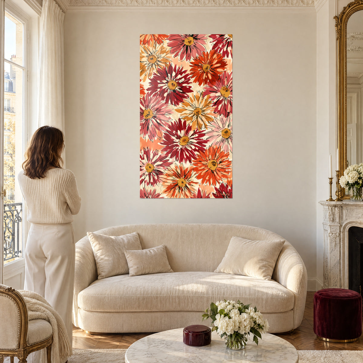 Cuadro de dalias carmín y naranja con corazones dorados, pétalos perfilados en negro, mujer de espaldas, sobre un sofá en un salón luminoso