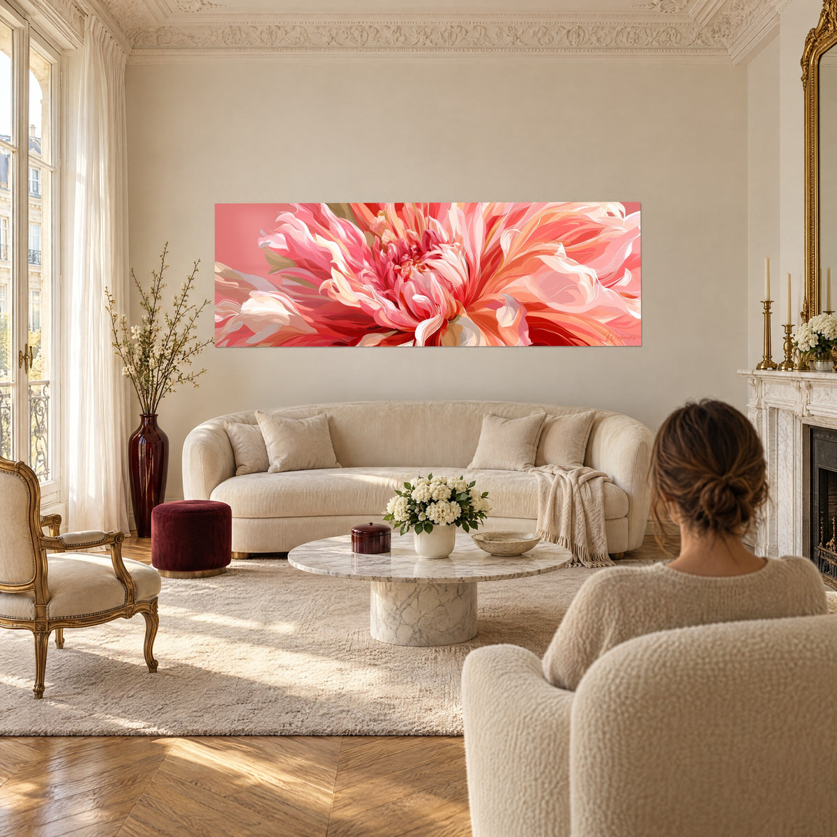 Wall art giant dahlia with coral and powdered pink petals, salmon background, hung near a woman seen from behind, above a sofa in a bright living room