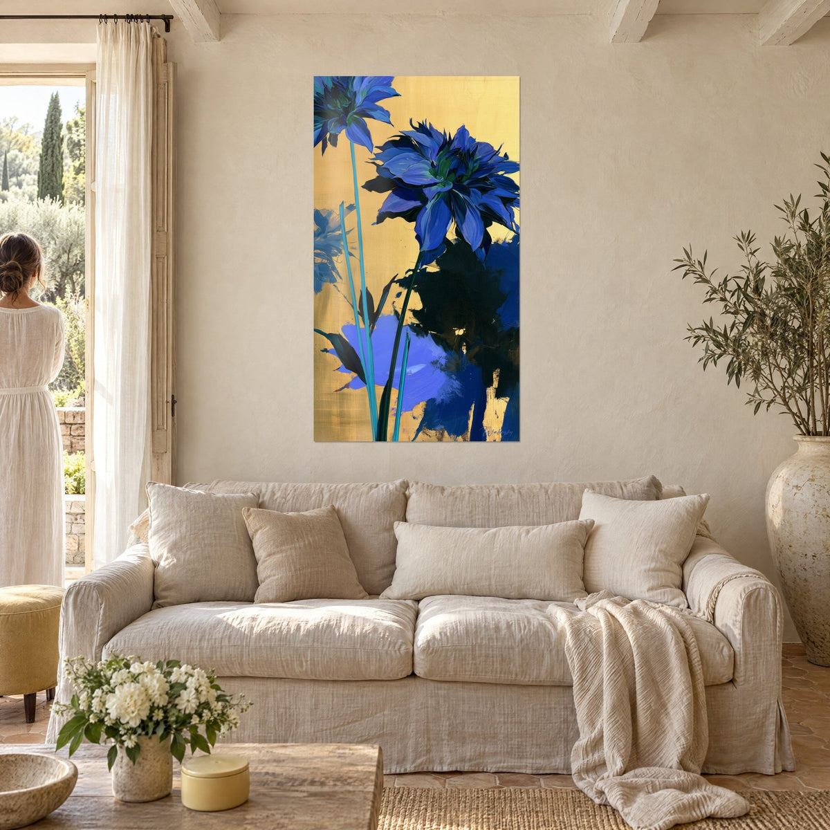 Tableau dahlia bleu cobalt sur fond or, tiges turquoise élancées, une femme de dos, au-dessus d'un canapé dans un salon lumineux