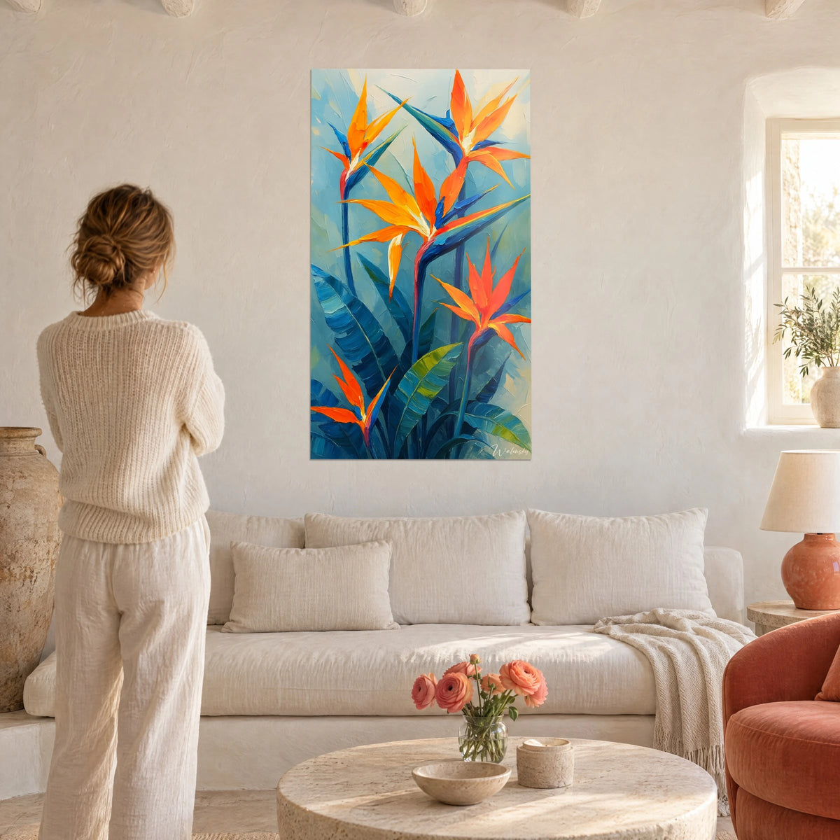 Wall art of orange bird of paradise flowers on a turquoise blue background, woman seen from behind, above a sofa in a bright living room
