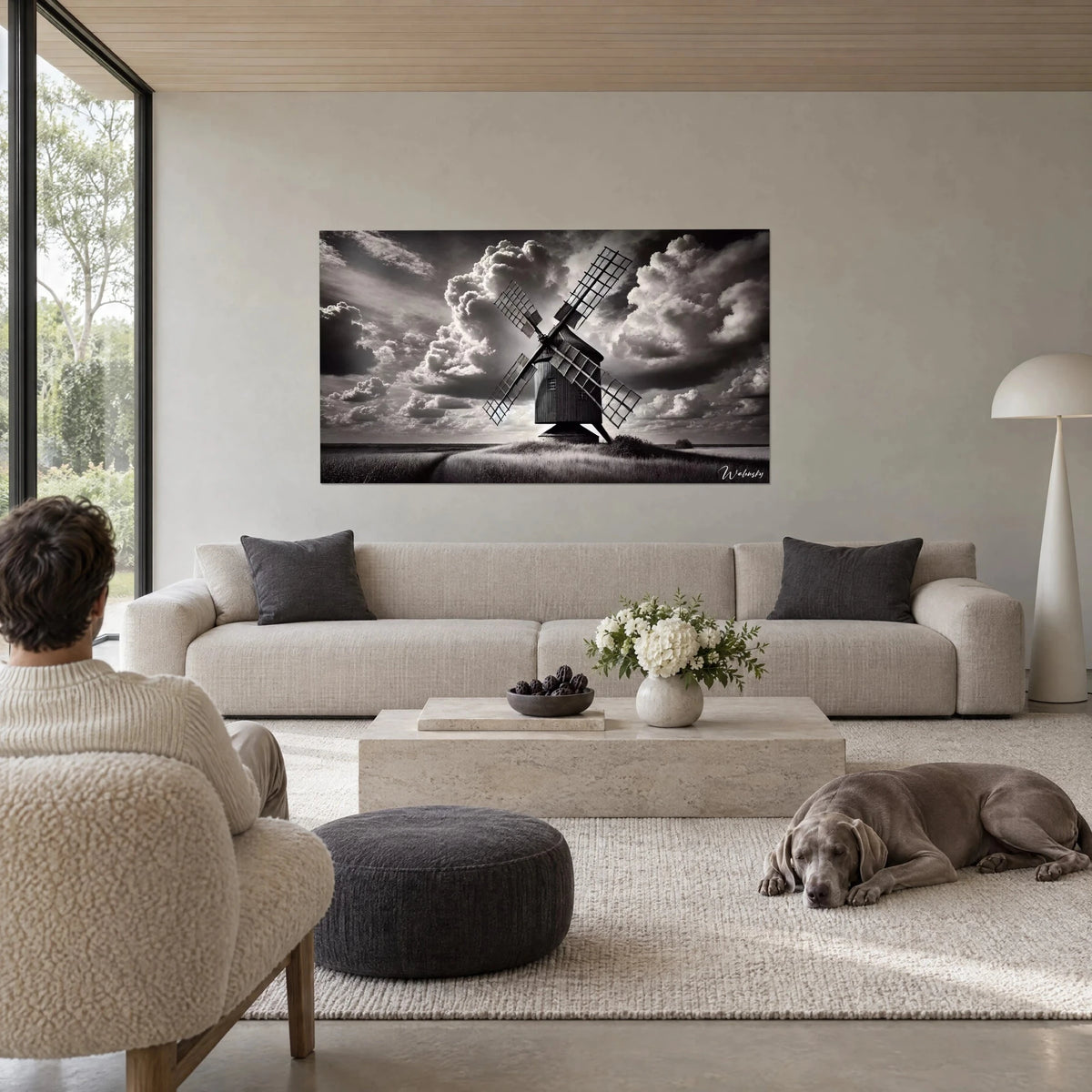 Quadro di un mulino nero sotto un cielo di tempesta grigio perla, pale a traliccio, cavallo grigio tranquillo in primo piano, sopra un divano in un soggiorno luminoso