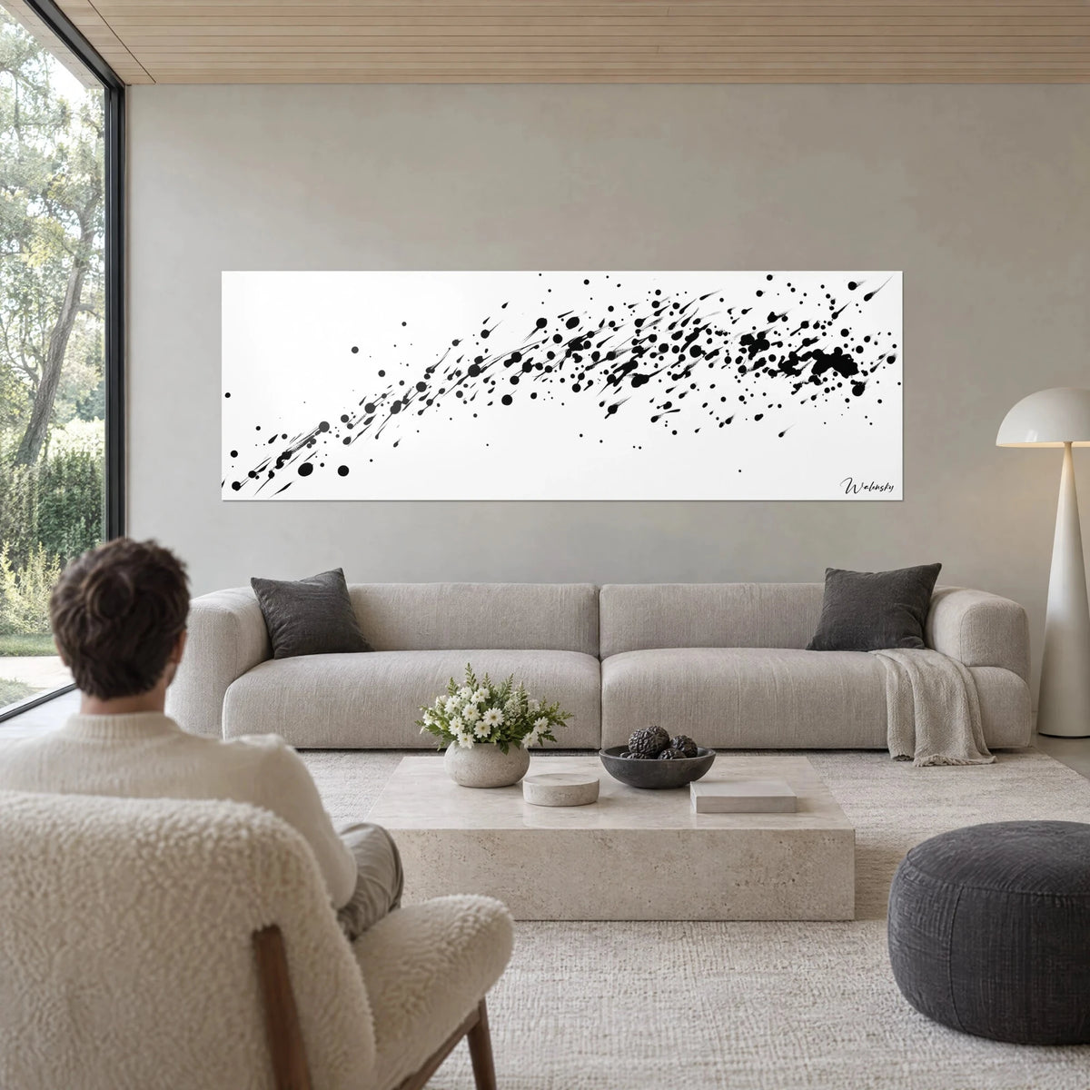 Quadro con schizzi di inchiostro nero in diagonale su fondo bianco puro, colature che scorrono, persona di spalle, sopra un divano in un soggiorno luminoso