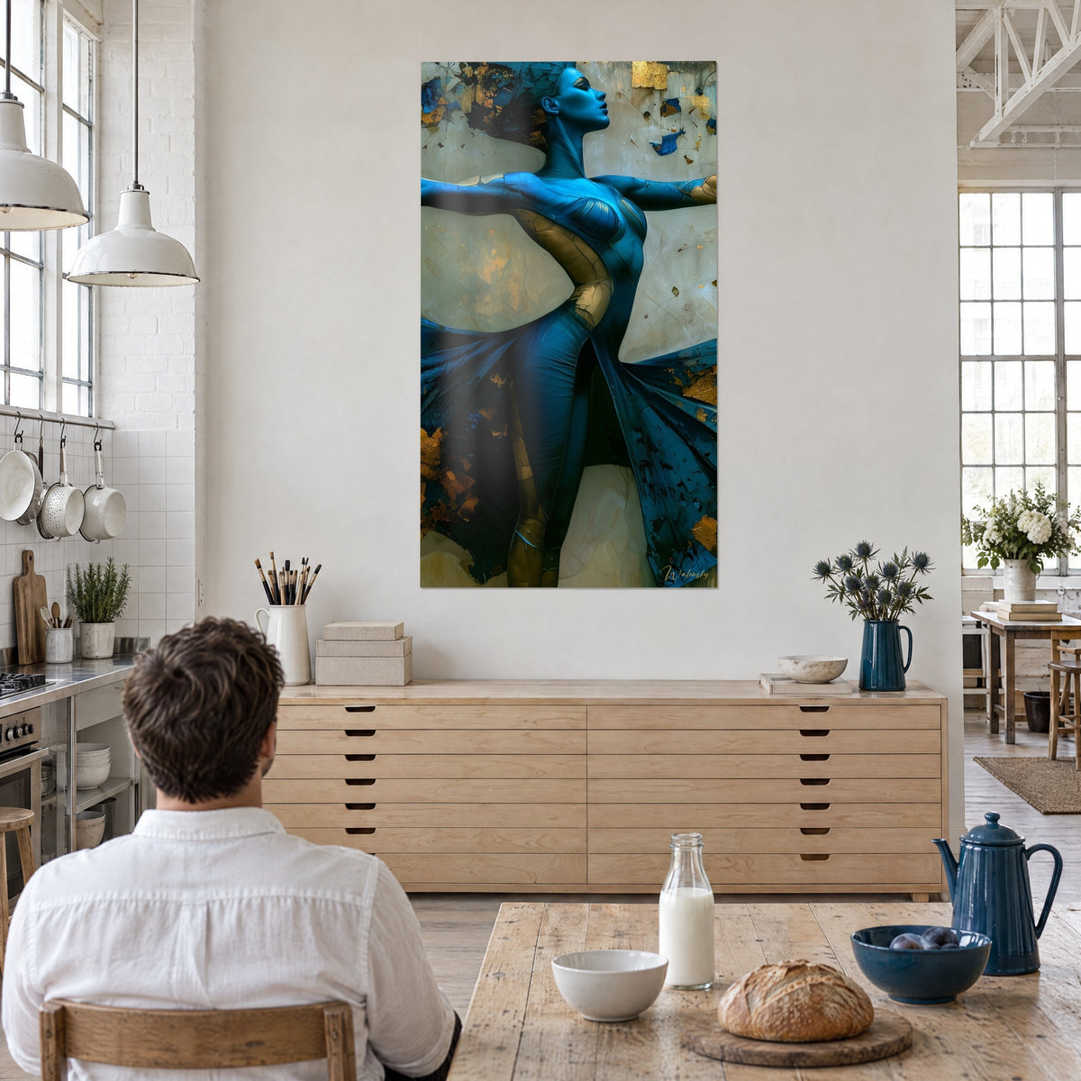 Wall art cobalt blue female figure, ivory fabric wings and flaking gold leaf, facing a man seated at a table in a loft kitchen