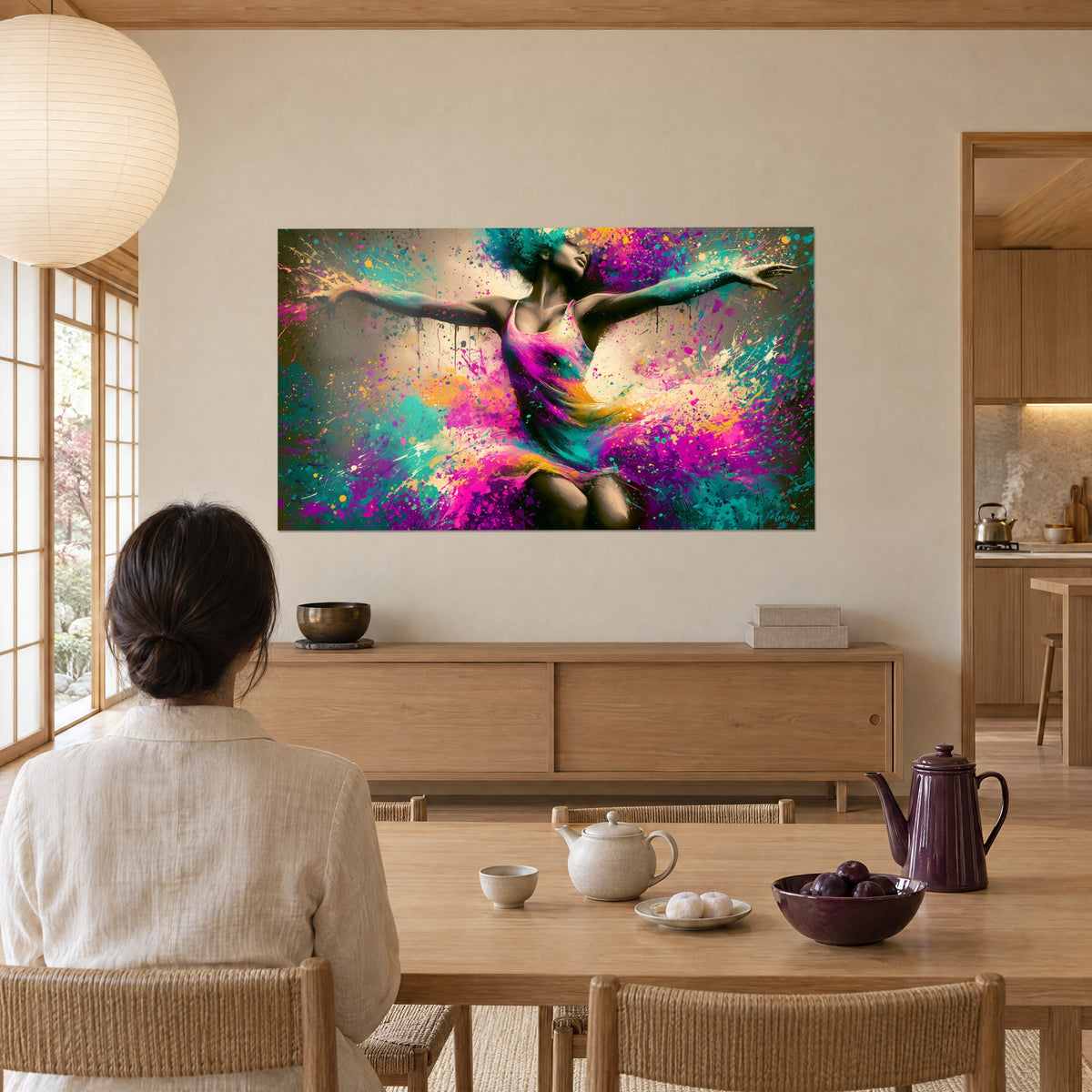 Schilderij dansende figuur omgeven door violette en saffraangele druppels, bekeken door een vrouw met de rug naar de kijker, zittend aan een tafel van licht hout